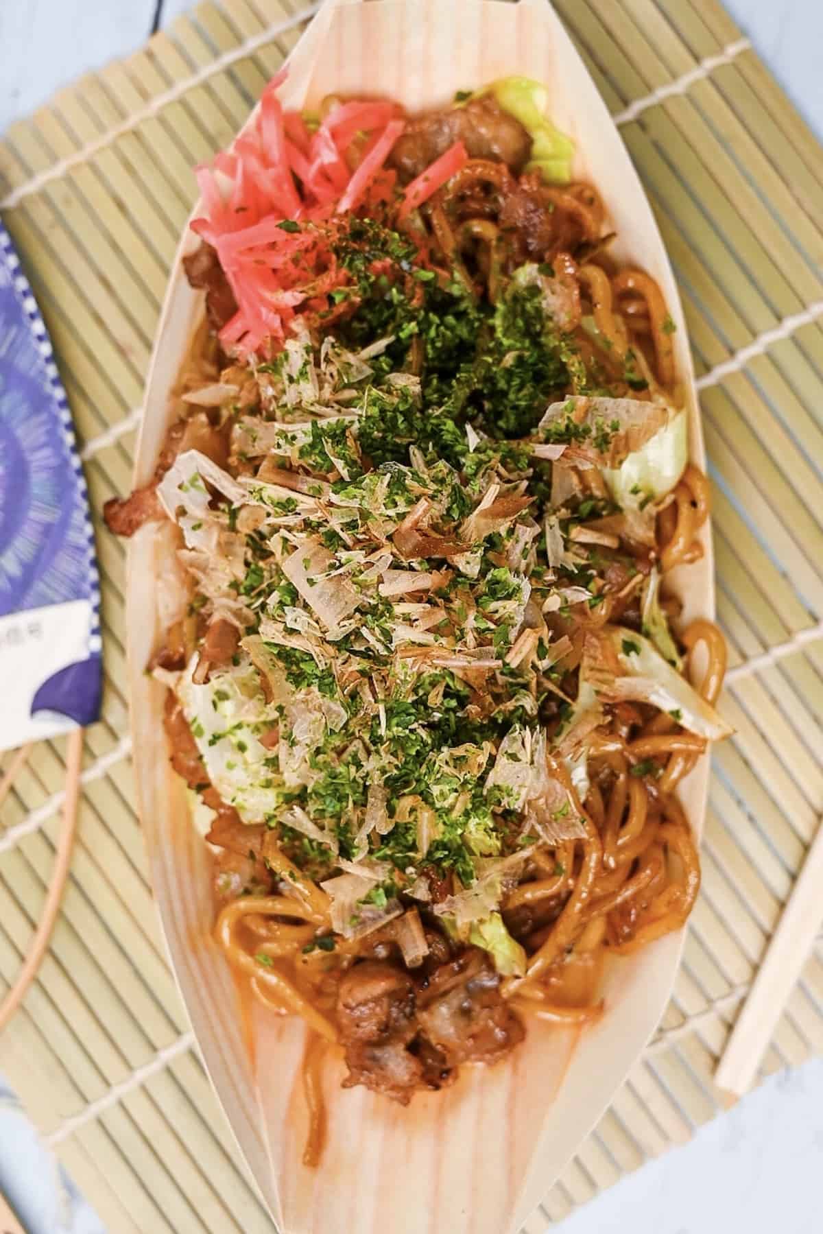 Festival style yakisoba served in a bamboo boat with red pickled ginger top down 