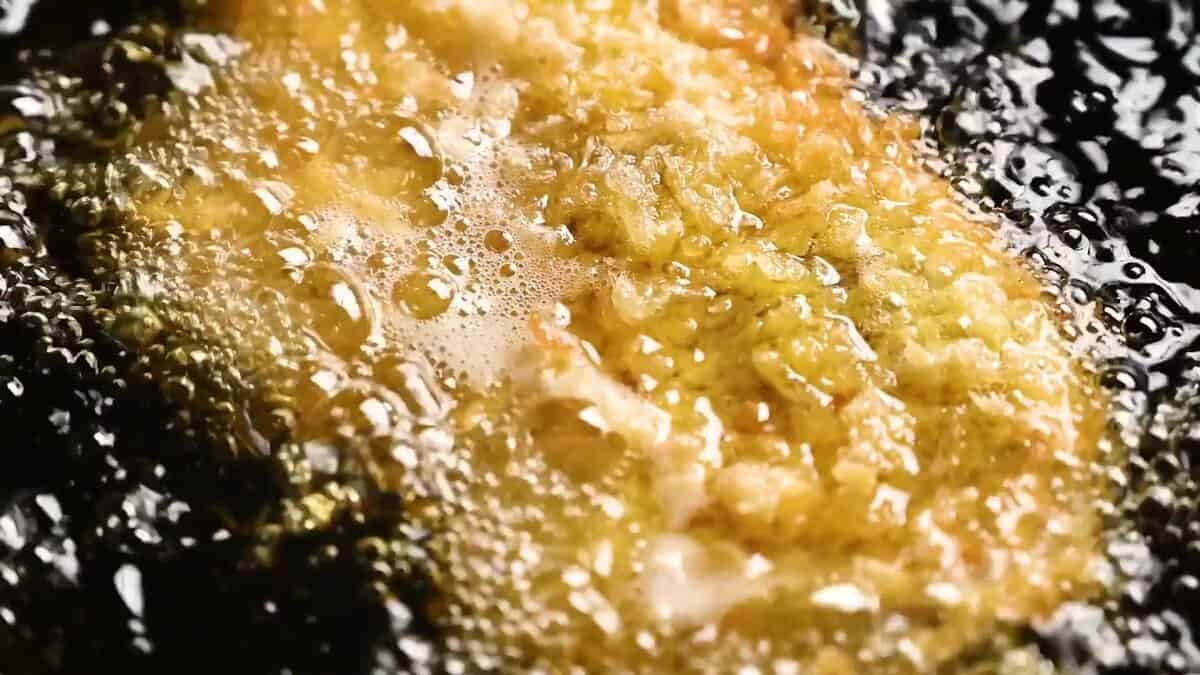 Close-up of tonkatsu frying with bubbling oil as the panko crust turns golden and crisp.