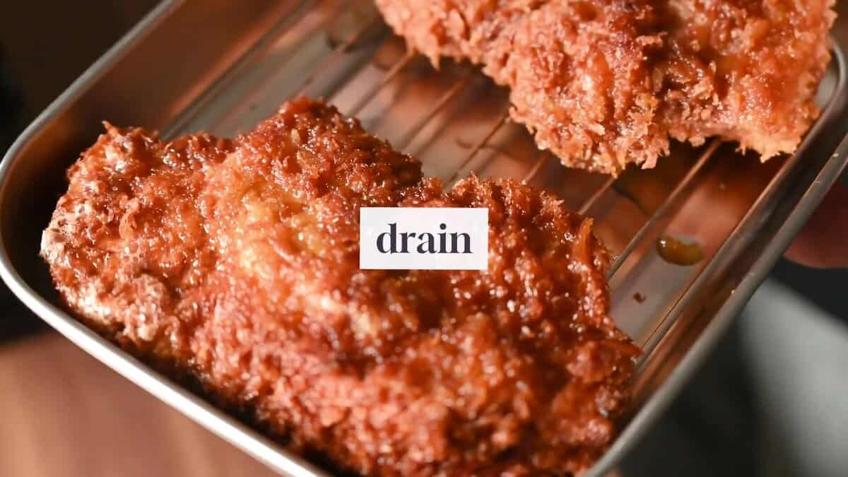 Golden-brown pork katsu draining on a rack after deep frying for a crisp panko coating.