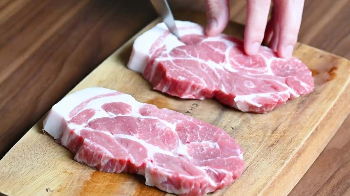 Hand scoring the fat and connective tissue on pork chops for tender, evenly cooked tonkatsu.