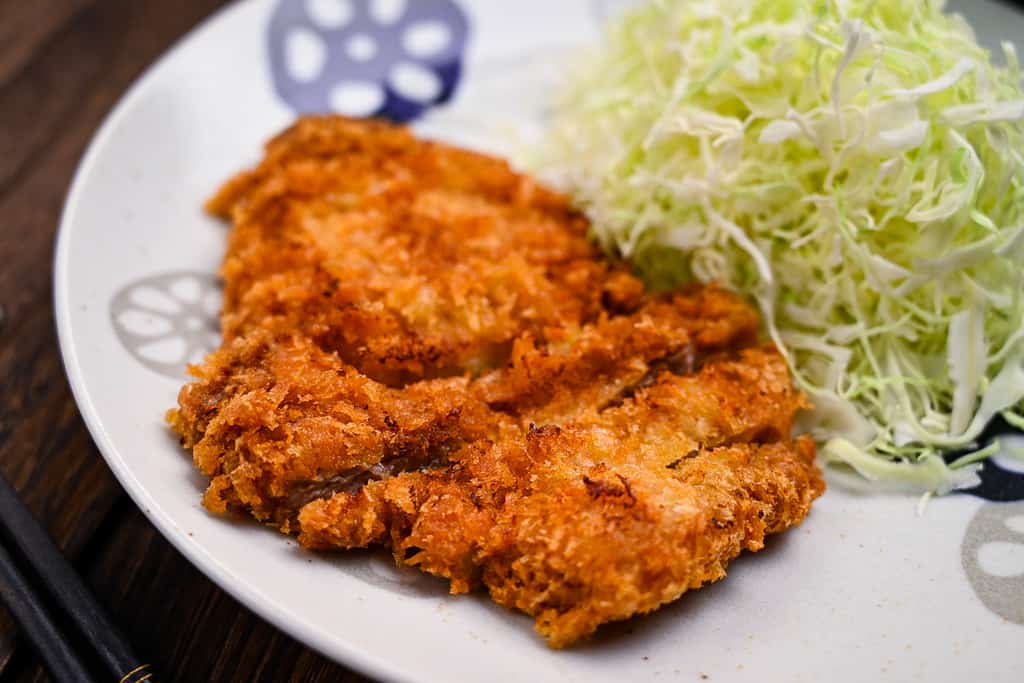 Japanese tonkatsu (deep fried pork cutlet) on a white plate with a mountain of cabbage