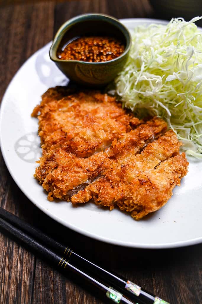 Japanese tonkatsu (deep fried pork cutlet) on a white plate with a mountain of cabbage and homemade dipping sauce