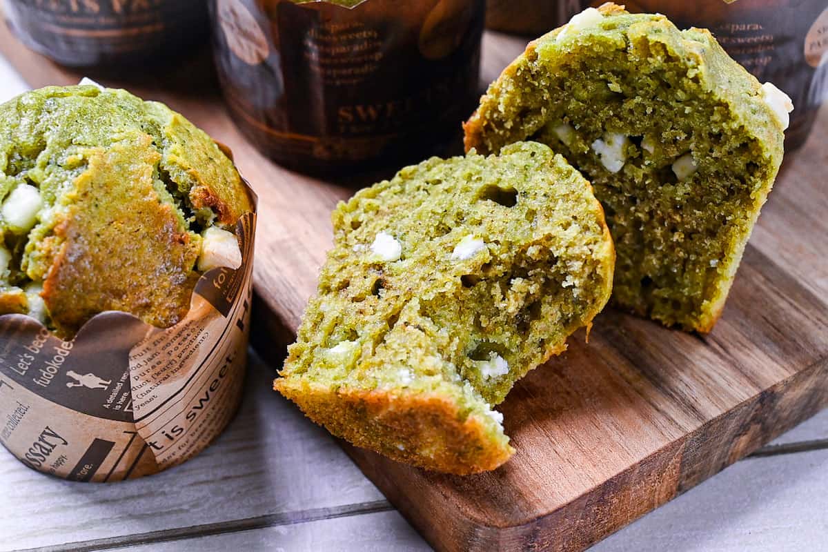 Matcha and white chocolate muffin cut in half with a bite missing on a wooden chopping board