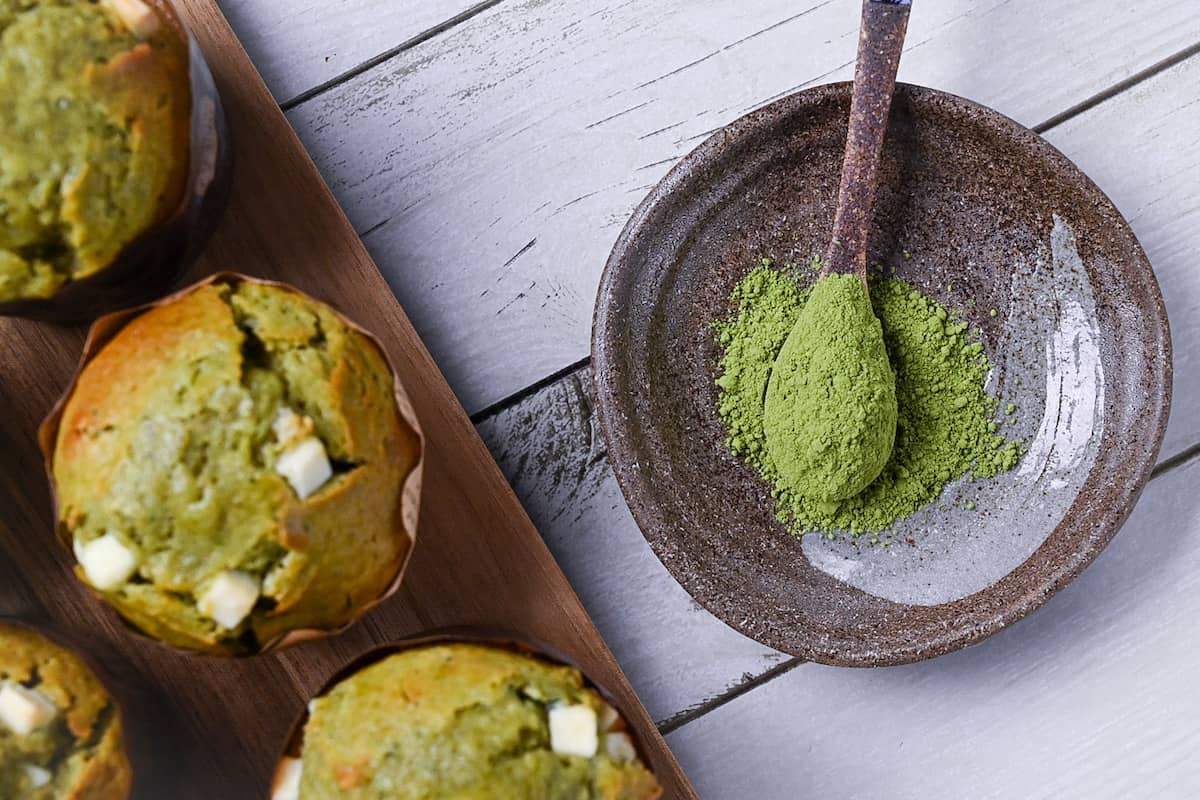 matcha muffins next to a small plate of matcha powder with ceramic spoon