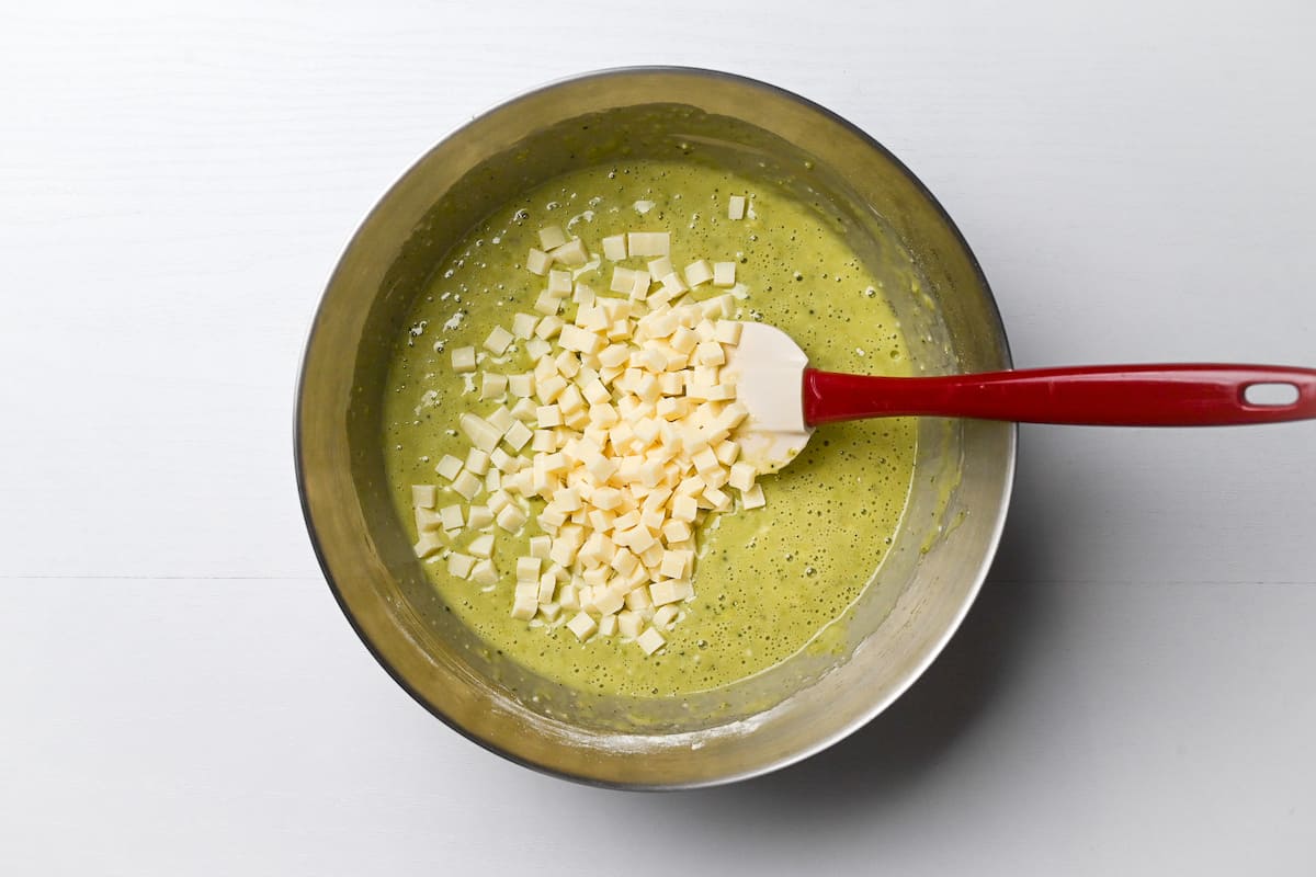 white chocolate chips added to matcha muffin batter in a mixing bowl