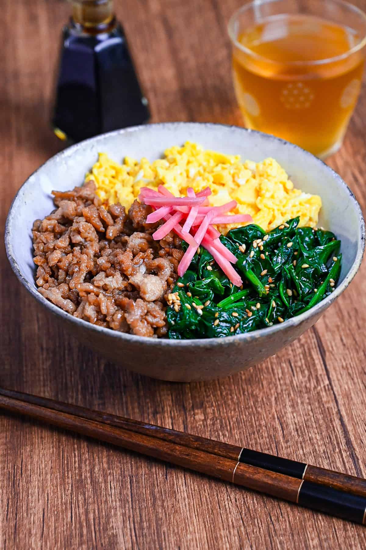 sanshoku don made with chicken soboro, scrambled egg and blanched spinach served over rice and topped with red pickled ginger on a wooden background
