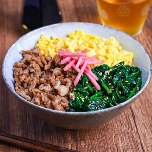 sanshoku don made with chicken soboro, scrambled egg and blanched spinach served over rice and topped with red pickled ginger on a wooden background