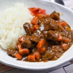 Japanese beef curry served on an oval white dish with a multi-colour wood effect background side view