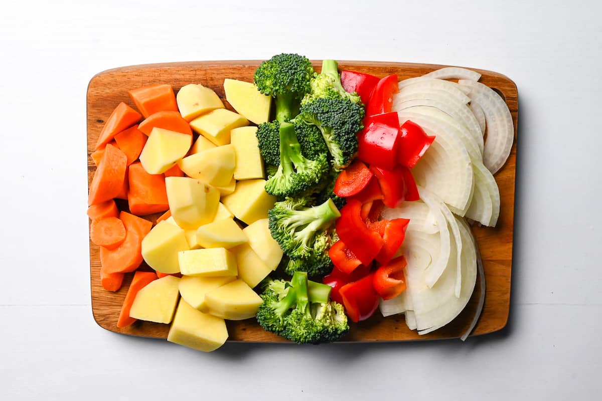 Cut carrots, potato, broccoli, bell pepper and onion on a wooden chopping board