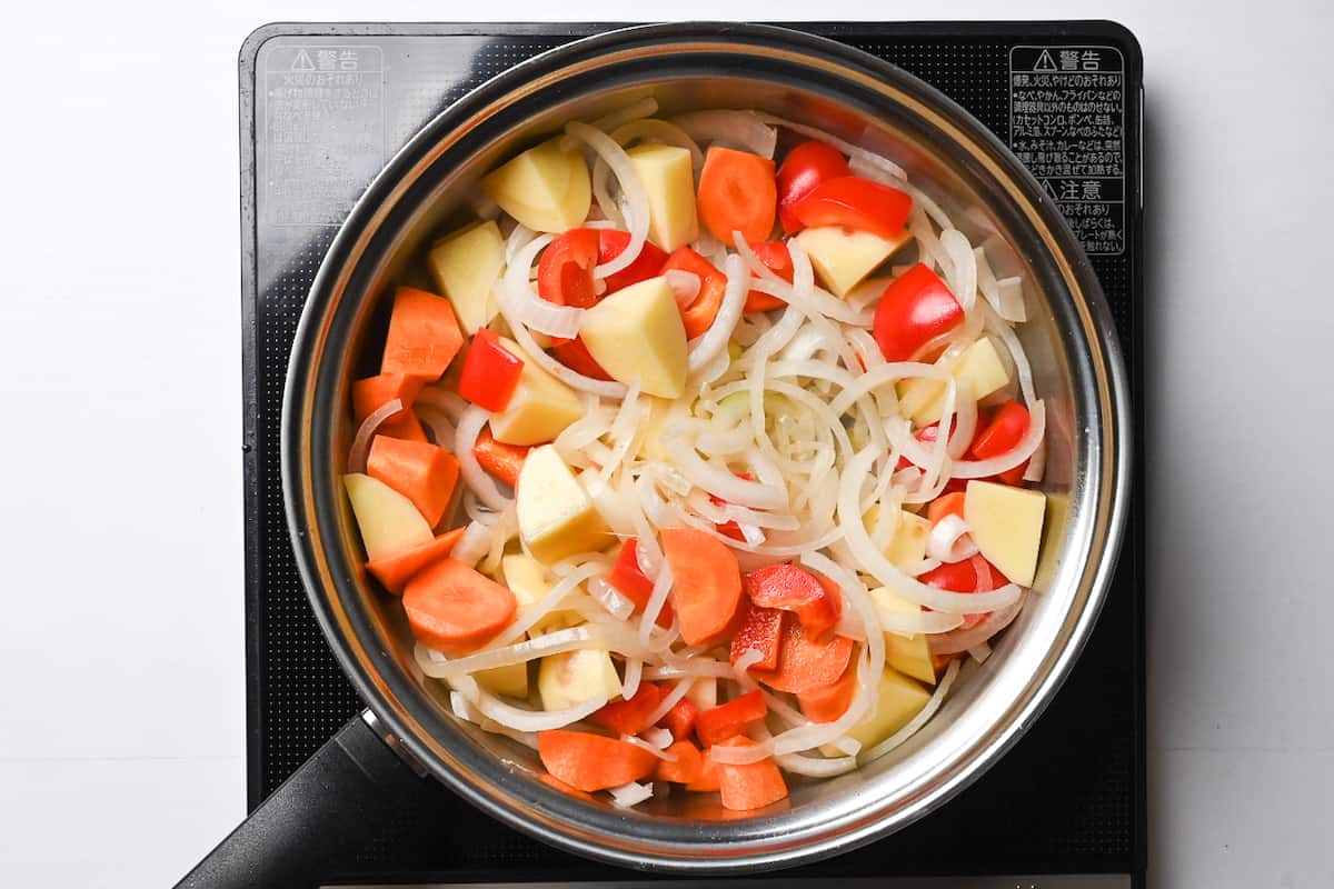 onion, carrot, bell pepper and potatoes cooking in a pan