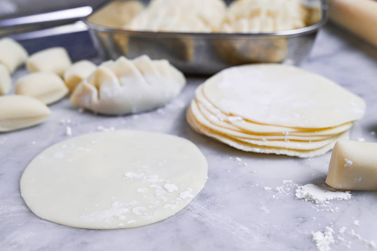 homemade gyoza wrappers in a stack next to a tray of homemade gyoza