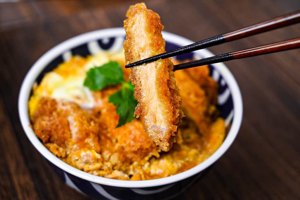 A piece of breaded pork tonkatsu held with chopsticks