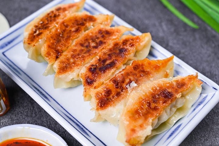 Japanese pan fried gyoza dumplings on a white plate with homemade dipping sauce