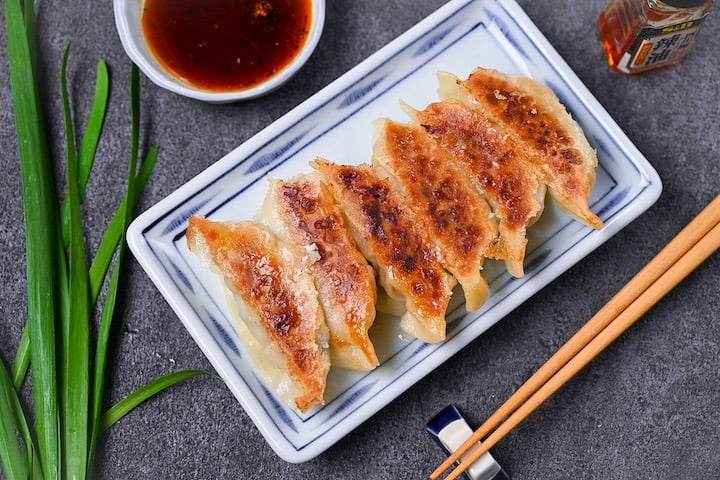 Japanese pan fried gyoza dumplings on a white plate with homemade dipping sauce