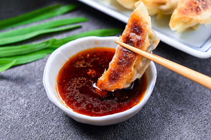 Japanese pan fried gyoza dumplings on a white plate with homemade dipping sauce