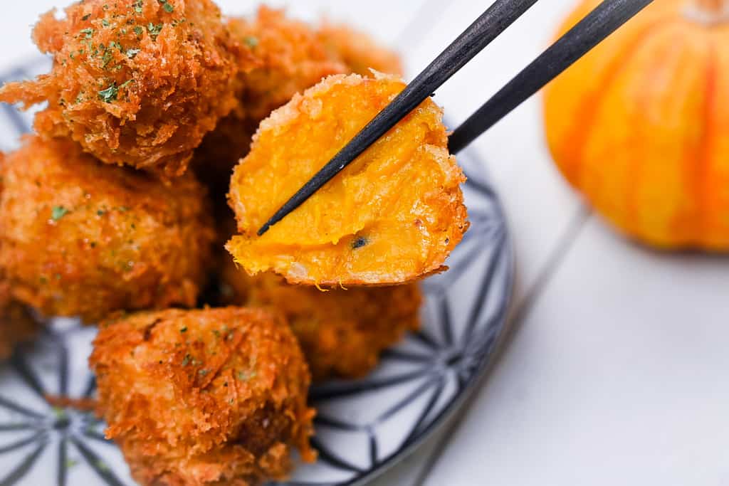 Japanese pumpkin croquette cut in half held with chopsticks