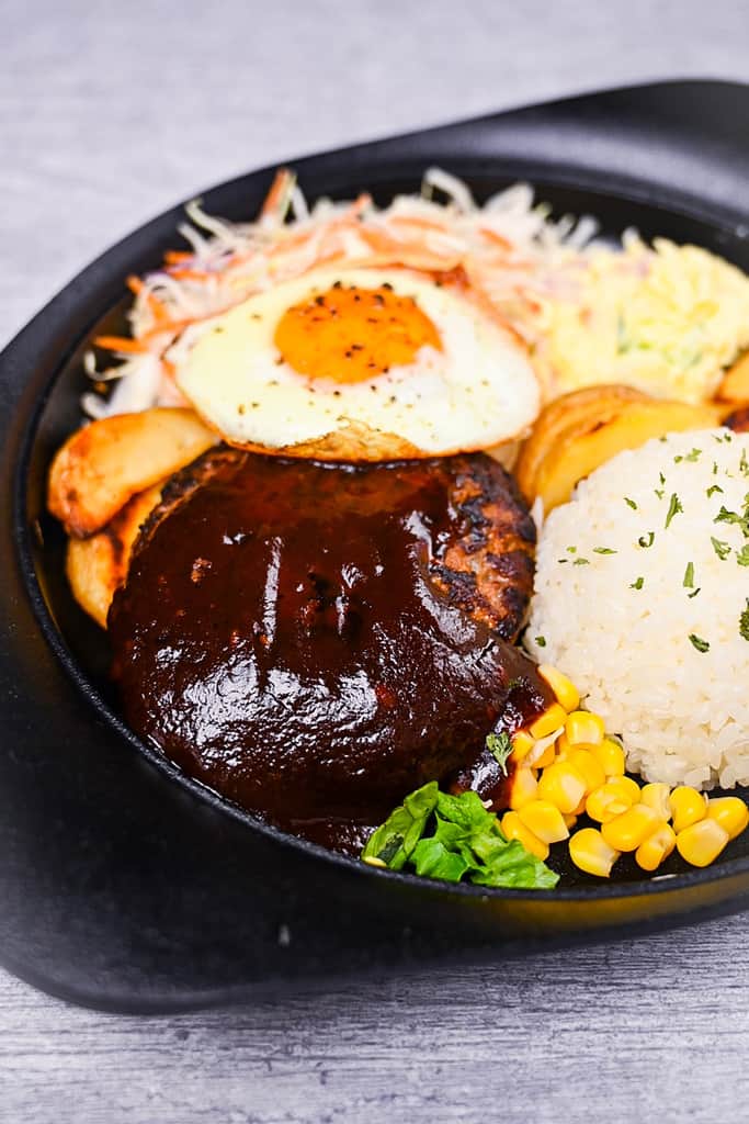 Japanese hamburg steak coated in sauce and served with rice, wedges, corn, salad and a fried egg