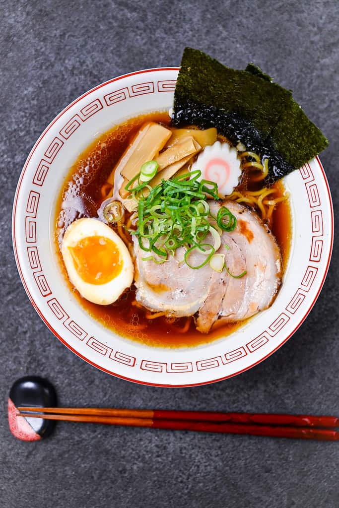 homemade Japanese chashu served in a bowl of shoyu ramen along with boiled egg, nori, narutomaki and spring onion top down portrait
