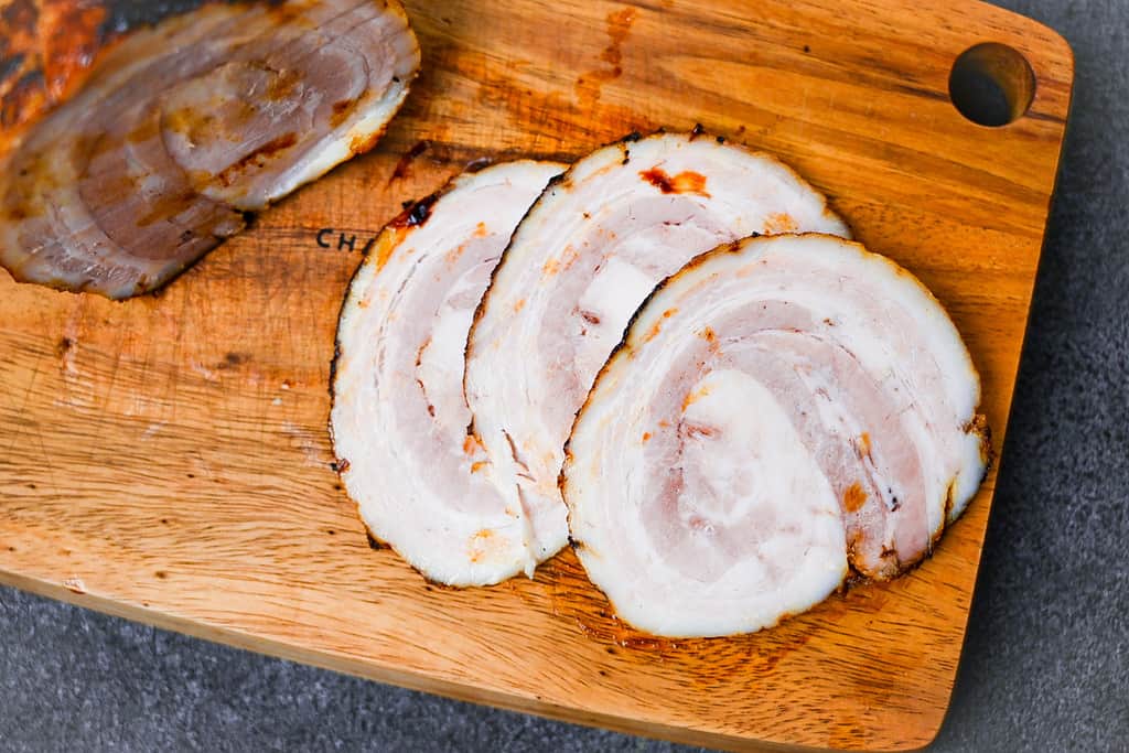 homemade Japanese chashu cut into three slices on a wooden chopping board top down view