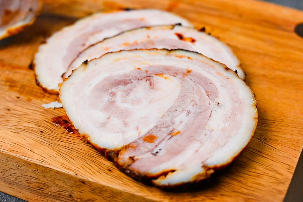 homemade Japanese chashu cut into three slices on a wooden chopping board close up