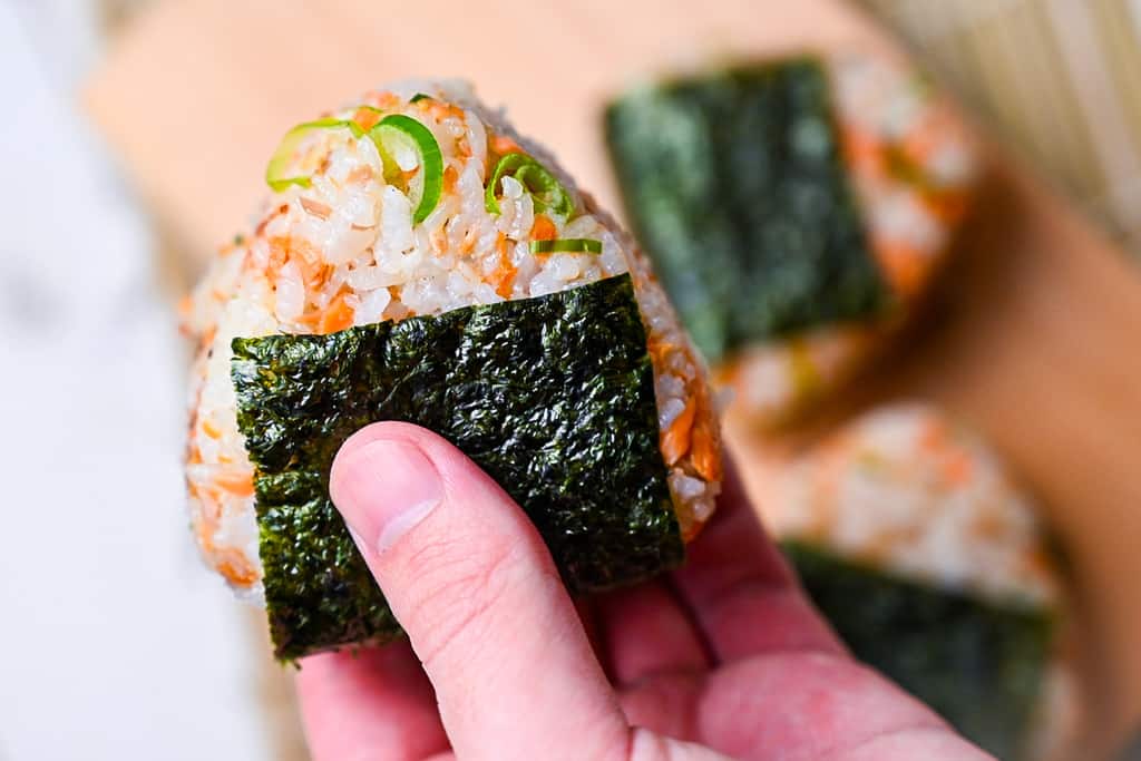 holding a salmon onigiri rice ball in hand