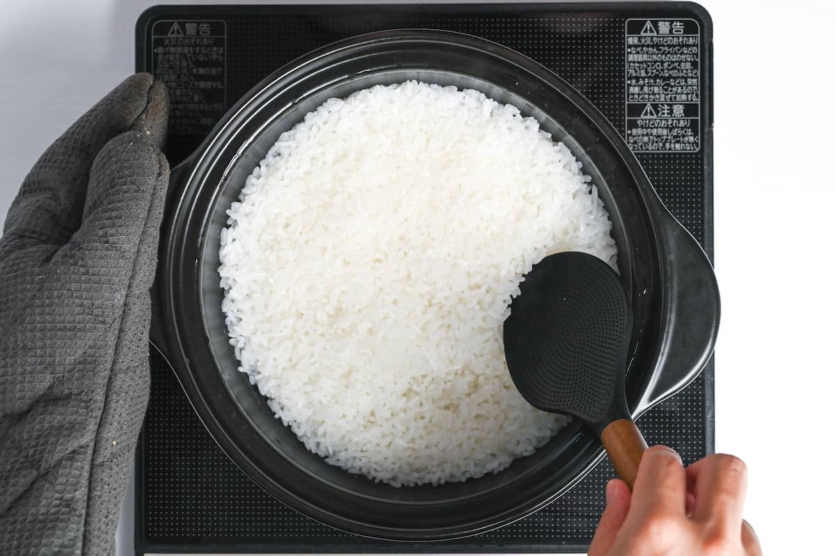 mixing rice in a black cooking pot with rice paddle