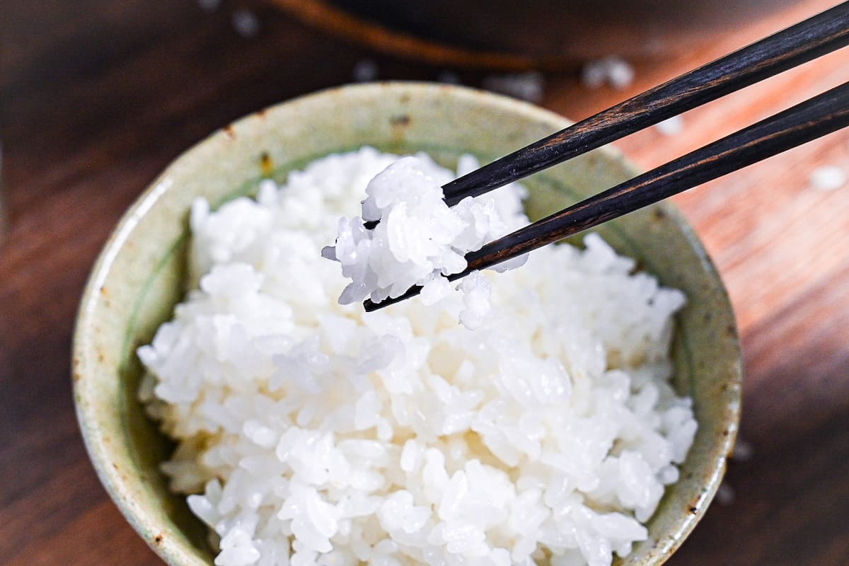holding cooked japanese rice with black chopsticks