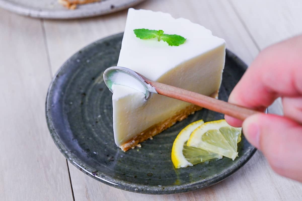 A slice of lemon rare cheesecake topped with a mint leaf and served on a dark green plate