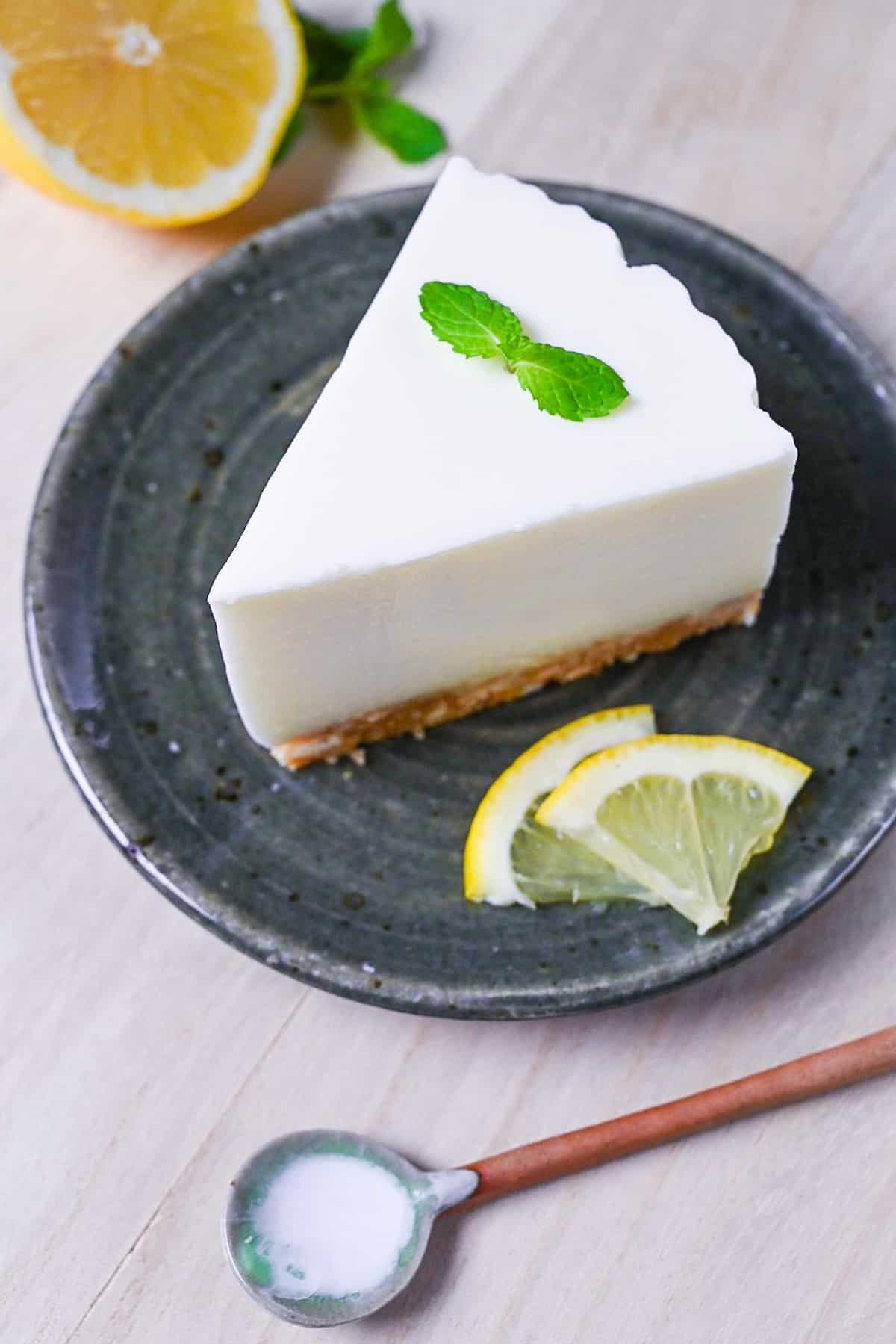 A slice of lemon rare cheesecake topped with a mint leaf and served on a dark green plate
