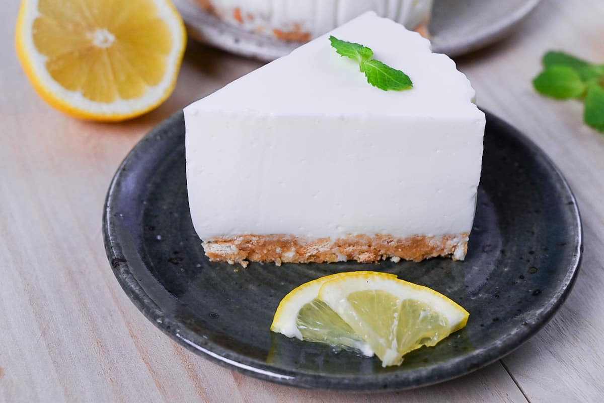 A slice of lemon rare cheesecake topped with a mint leaf and served on a dark green plate