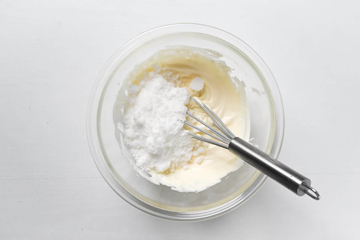 adding sugar to soft cream cheese in a glass bowl