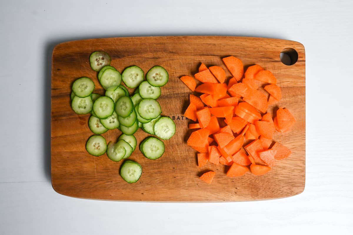 sliced cucumber and carrots on a wooden chopping board