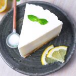 A slice of lemon rare cheesecake topped with a mint leaf and served on a dark green plate