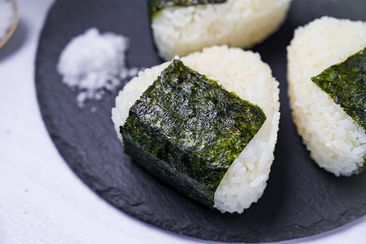 Three salted onigiri rice balls on a round slate plate