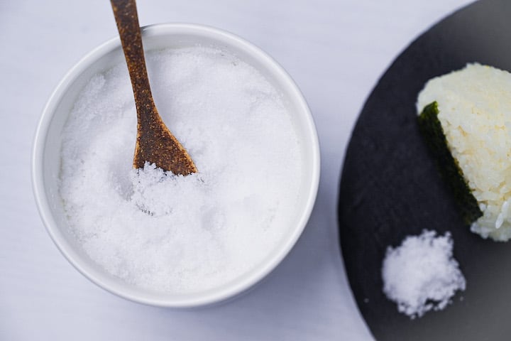 Salt in a white jar with brown ceramic spoon