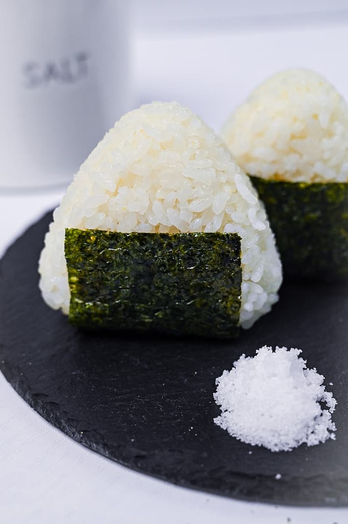 Two salted onigiri rice balls on a round slate plate