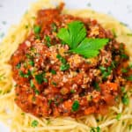 Spaghetti meat sauce served on a white plate and sprinkled with Italian parsley close up