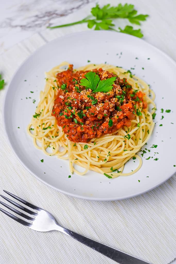 Spaghetti meat sauce served on a white plate and sprinkled with Italian parsley side view