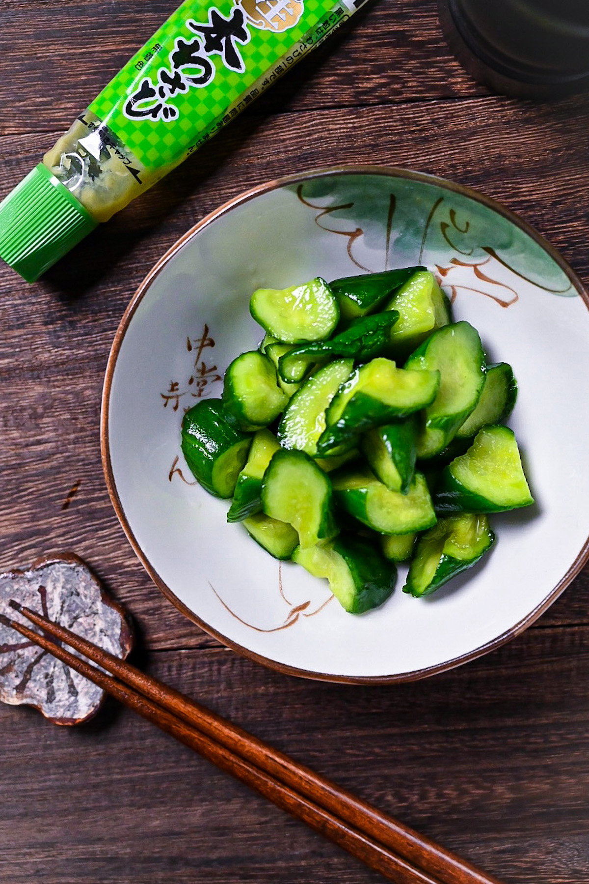Japanese wasabi pickled cucumbers in a white dish with chopsticks and a tube of wasabi paste