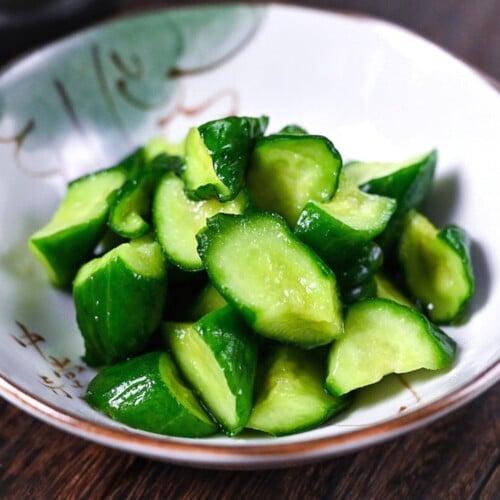 Japanese wasabi pickled cucumbers in a white dish with chopsticks and a tube of wasabi paste