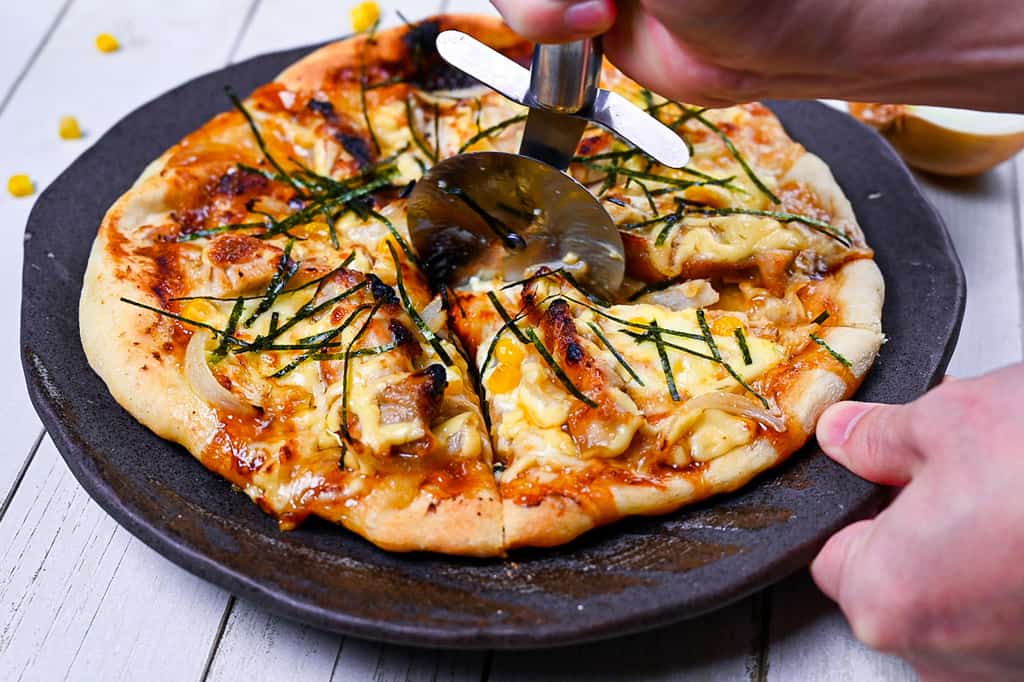 Cuttng Japanese Teriyaki Chicken pizza with a pizza cutter