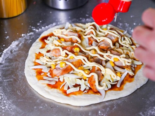 drizzling mayonnaise over teriyaki chicken pizza