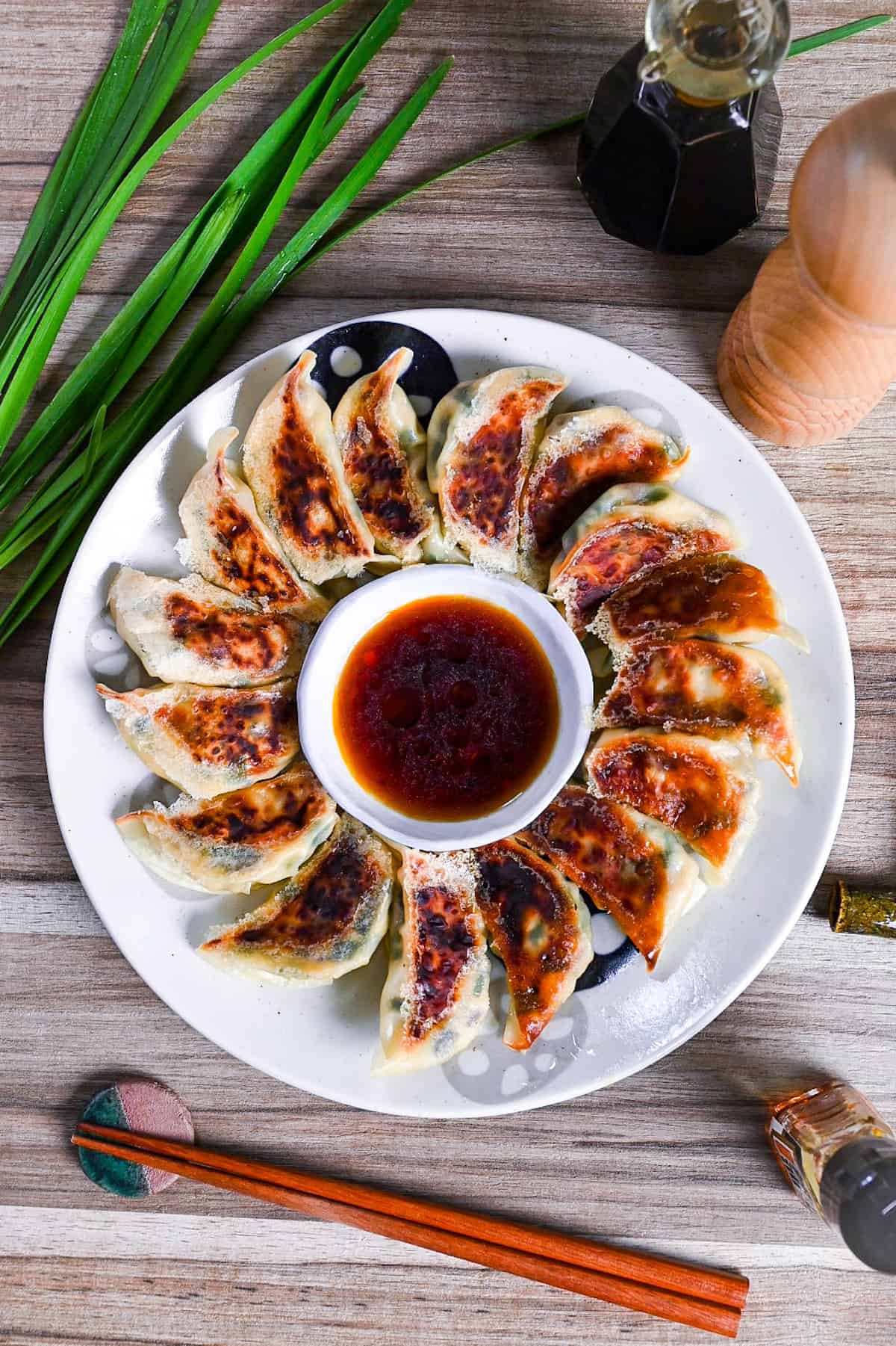 pan-fried tofu and vegetable gyoza on a white plate arranged in a circle around a bowl of gyoza dipping sauce