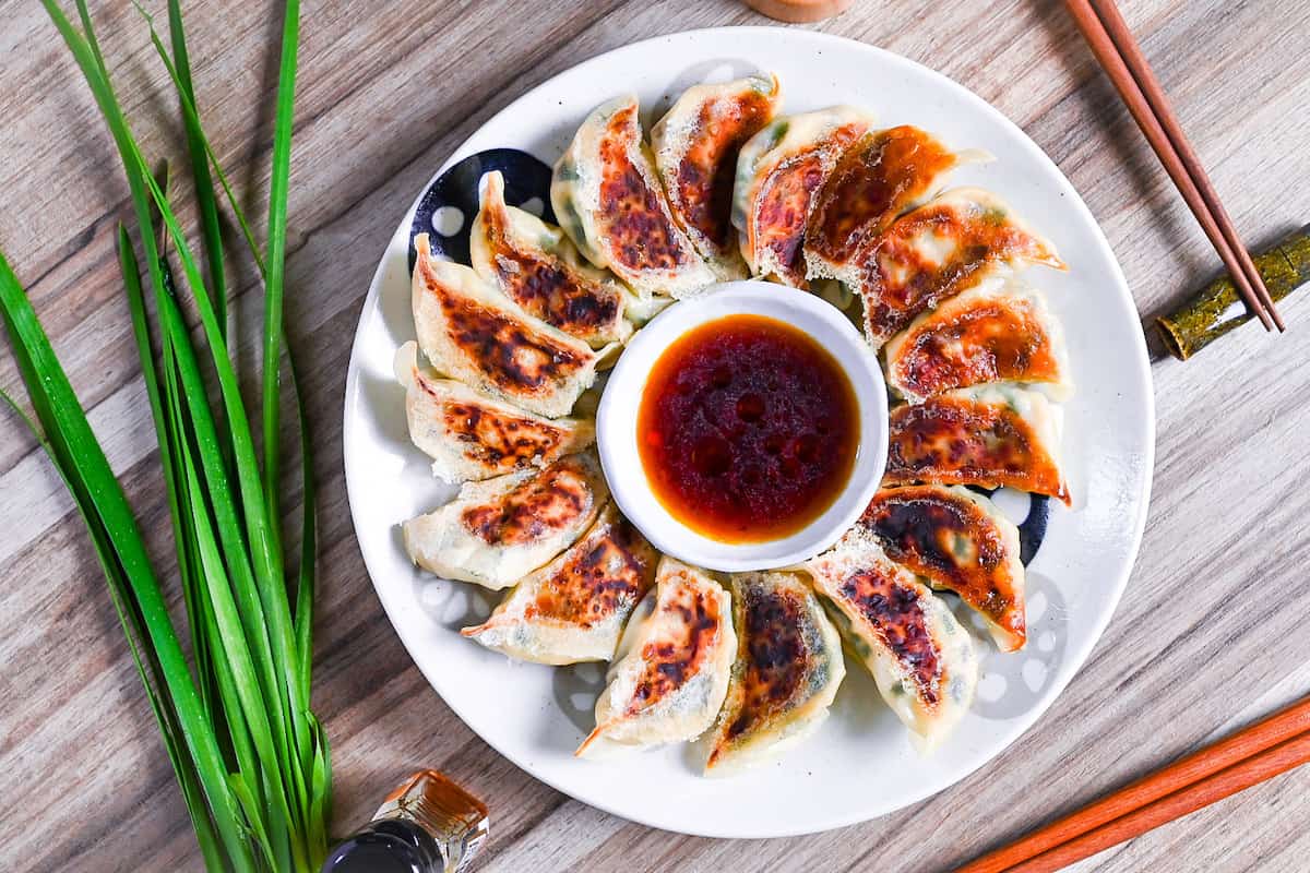 pan-fried tofu and vegetable gyoza on a white plate arranged in a circle around a bowl of gyoza dipping sauce