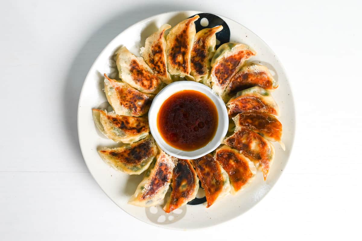 pan-fried tofu and vegetable gyoza on a white plate arranged in a circle around a bowl of gyoza dipping sauce
