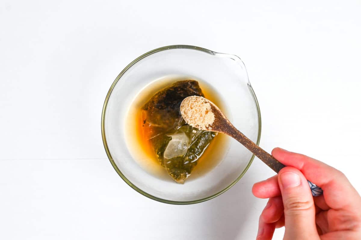 adding light brown sugar to hojicha and hot water in a bowl