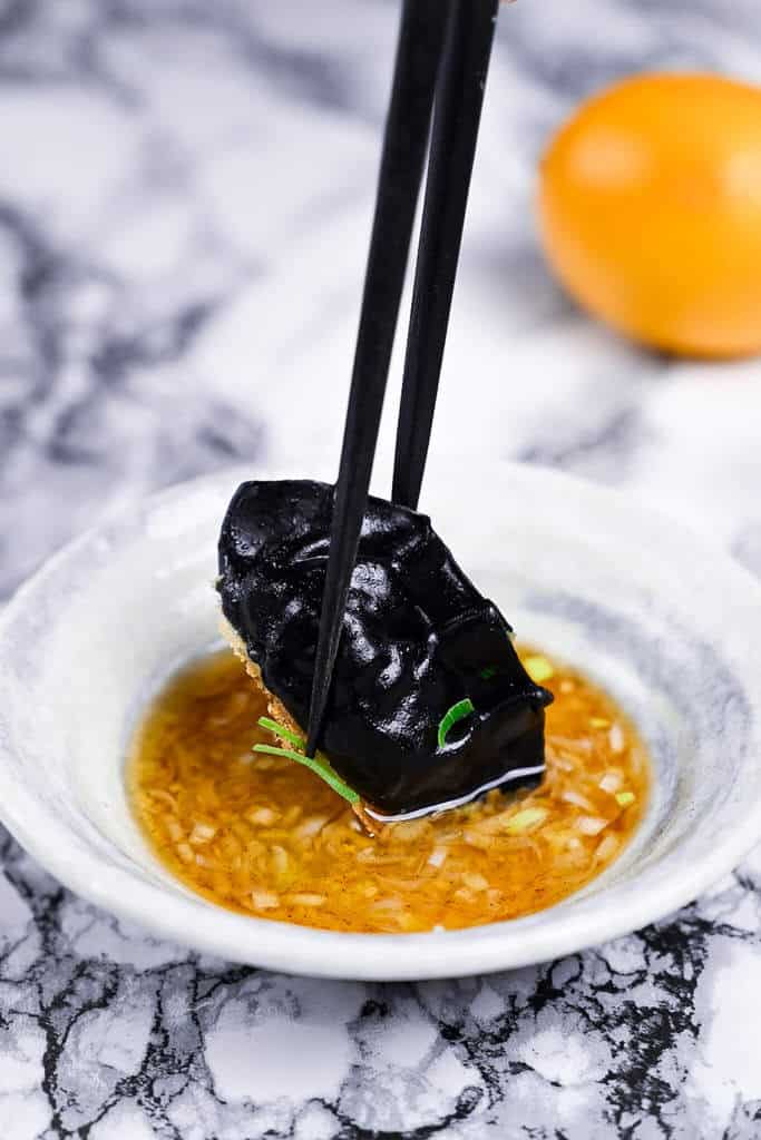 dipping squid ink gyoza in sauce