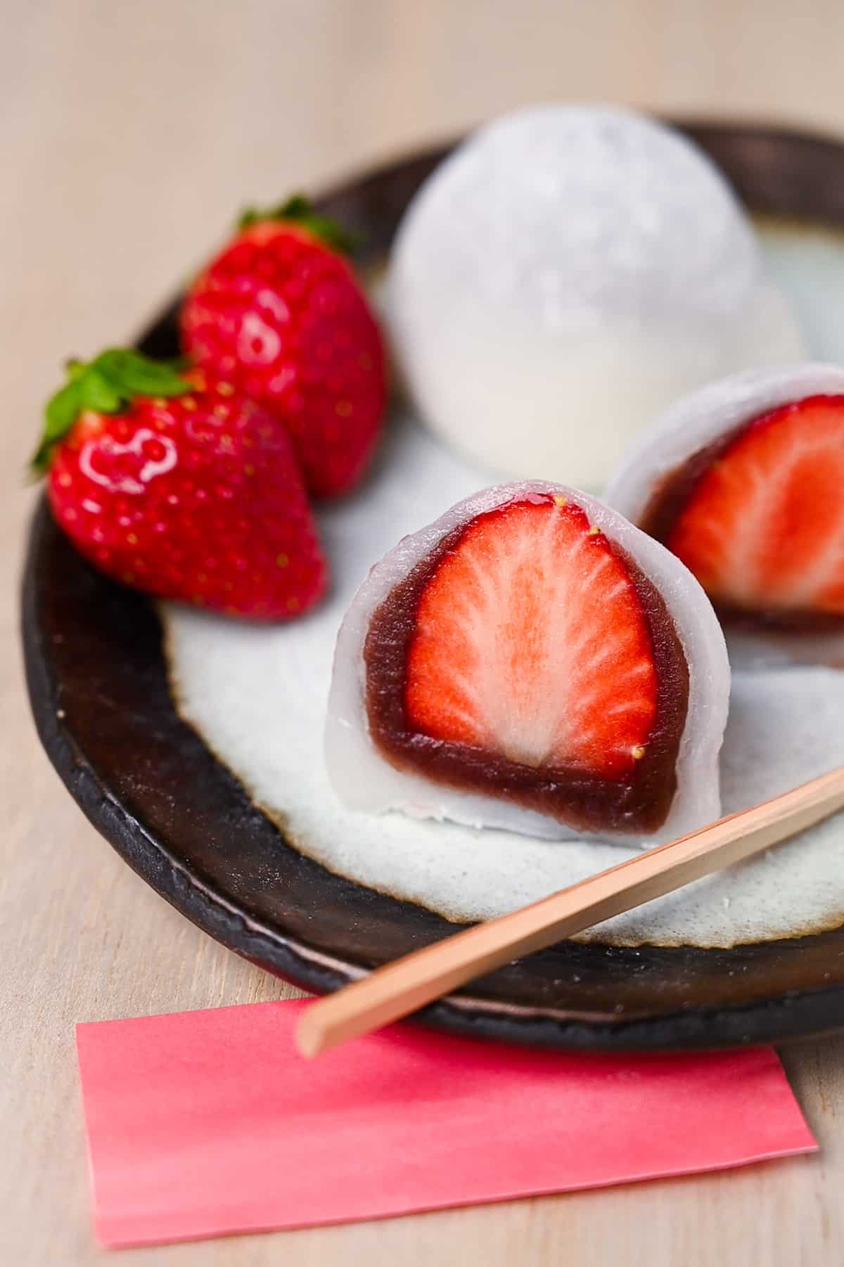 Homemade ichigo daifuku (strawberry mochi) cut in half and served on a plate with strawberries