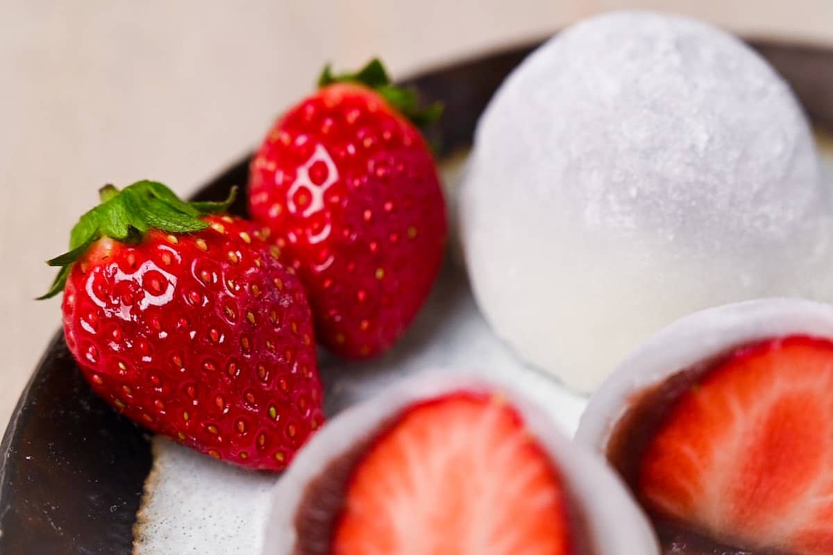 Homemade ichigo daifuku (strawberry mochi) cut in half and served on a plate with strawberries