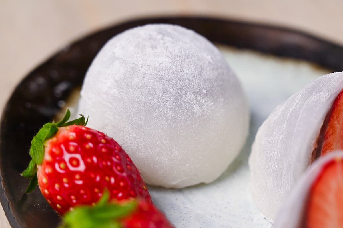 Homemade ichigo daifuku (strawberry mochi) cut in half and served on a plate with strawberries